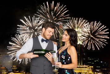 celebration and holidays concept - happy couple with bottle of non alcoholic champagne and wine glass at party over firework lights at night city background