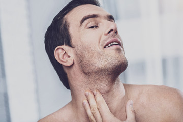 Skin care. Close up of charismatic unshaven man standing in front of the mirror and looking at the...