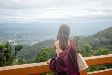Fototapeta na wymiar The Asian woman is looking to the city and mountain view from the balcony in Thailand. 