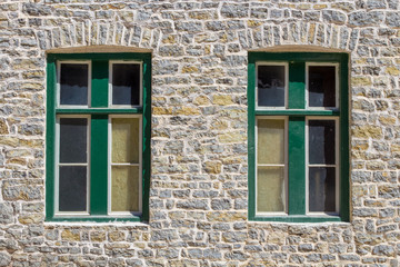 Two green windows in a stone brick wall of an old house