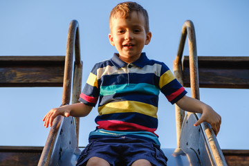 summer, childhood, friendship and people concept - happy little boy on children playground slid...