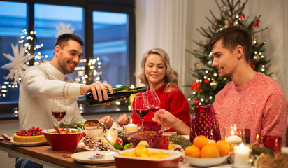 holidays and celebration concept - happy friends having christmas dinner at home and drinking red wine
