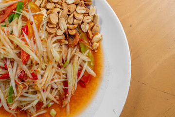 The close up of papaya salad with long bean tomato and peanut in the white dish on the wooden table. 