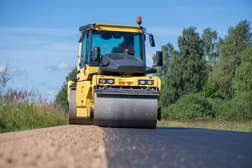 Yellow heavy vibration roller at asphalt pavement works. Road repairing in city. Road construction workers repairing highway road on sunny summer day. Heavy machinery, loaders and trucks