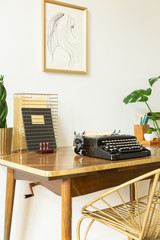 Chair at wooden desk with typewriter in classic workspace interior with poster on white wall. Real...