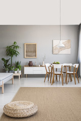 Pouf on brown carpet in spacious grey flat interior with chairs at table and posters on the wall. Real photo