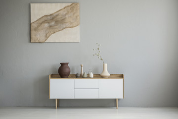 Poster on grey wall above white cupboard with vase in minimal living room interior. Real photo