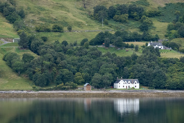 Fototapeta na wymiar Loch Broom, Inverness, Scotland. White painted house on the shore of the loch, reflected in the water. 