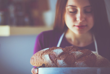 Young woman holding tasty fresh bread in her kitchen