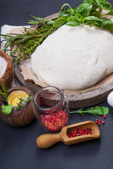 Wooden rolling pin with freshly prepared dough and dusting of flour on dark background