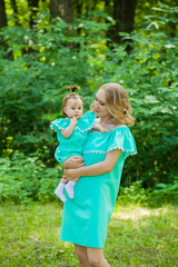 Fototapeta premium a young mother on a walk with a baby. Mom and daughter in identical dresses. Keep the baby in your arms
