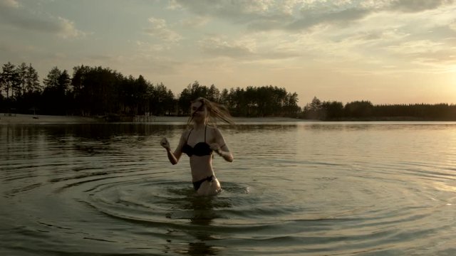 Beautiful girl, blond, funny dancing in the water of a forest lake and laughing.