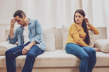 Domestic problem. Sad male person sitting on the couch and touching his forehead while being deep...