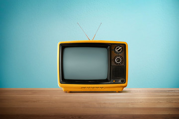 Ancienne télévision rétro vintage de couleur orange jaune sur table en bois avec fond bleu menthe.