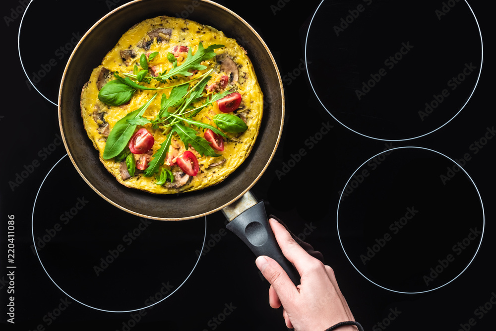 Wall mural cropped shot of woman cooking omelette in frying pan on black stove