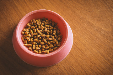 Cat food in a red plastic bowl on wooden background.