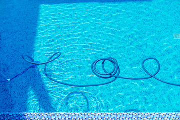 Man cleaning the swimming pool with vacuum equipment.