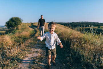 adorable happy little boy running on rural path while father walking behind