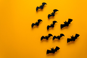 Black paper bats flying on yellow background. Halloween concept. Paper cut style. Top view