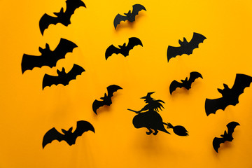 Witch on broom and black paper bats flying on yellow background. Halloween concept. Paper cut style. Top view
