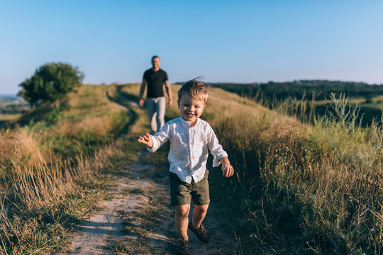 adorable happy little boy running on rural path while father walking behind