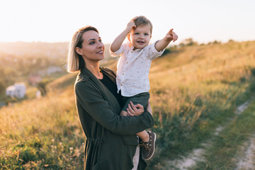 happy young mother carrying adorable little son pointing with finger outdoors