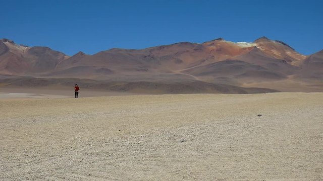 A traveler in the desert of Bolivia, next to the atacama desert in Chile, running far away from the camera.