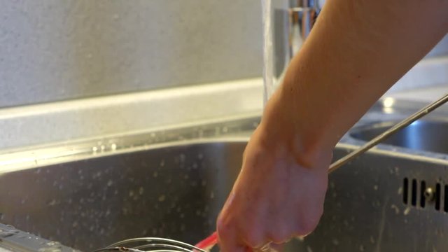 Woman washing a silicone spatula in a sink under a hot water.