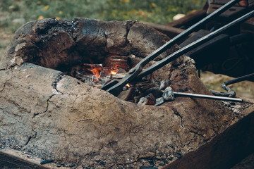 Close up of medieval furnace with iron tongs, burning coals and fire in blacksmith forge