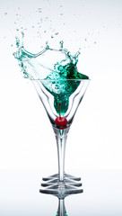 Red cherry dropped into a martini glass filled with a green drink creating a splash