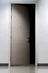 The mysteriously open door to the dark room. Illuminated corridor of a residential house with open door to the apartment without light.