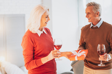 Anniversary celebration. Joyful female person standing in semi position while looking at gift box