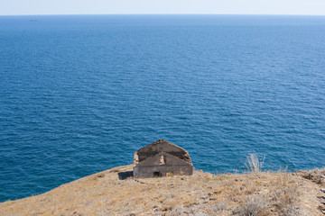 old destroyed single house without a roof on a cliff face overlooking the sea