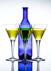 Three martini glasses in front of a blue bottle against a white background. Glasses filled with a yellow drink