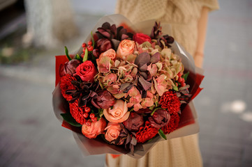 Woman in beige dress holding a romantic bouquet of flowers in red tones