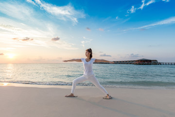 Beautiful Attractive Asian woman practicing yoga warrior or Virabhadrasana Pose on the beach in Maldives with sunset,Feeling so comfortable and relax in holiday