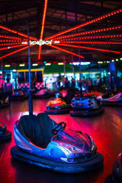Front view from bumper cars in an amusement park. In this photo: Stopped bumper cars, neon lights, fun, no people and night photo.