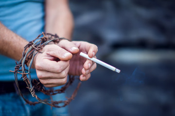 Cigaret in hands with barbed wire on a dramatic background. Concept of drugs, smoking addiction.