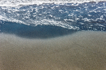 sea waves on black sand near water on the beach. Background texture.