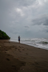 man walking on the beach with dark sand