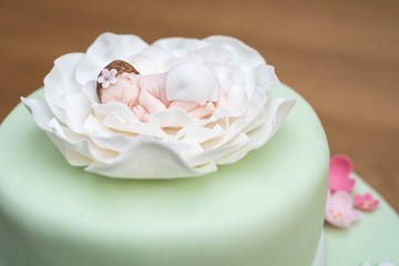 Fototapeta na wymiar Cloes up of green baptism cake with green fondant and a baby on top in a white flower