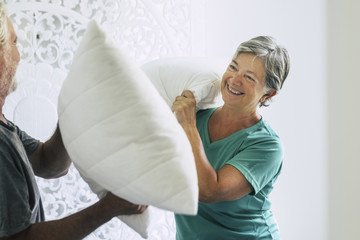pillows war at home for caucasian couple of playful adult senior man and woman play in the bedroom...