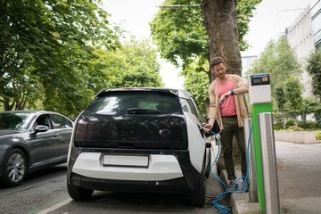 Man checking time on smart watch while charging electric car