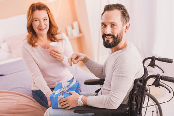 Inclusive life. Paralyzed cheerful man smiling and opening his birthday present