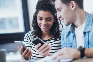 Look at this. Positive two friends smiling while using phones