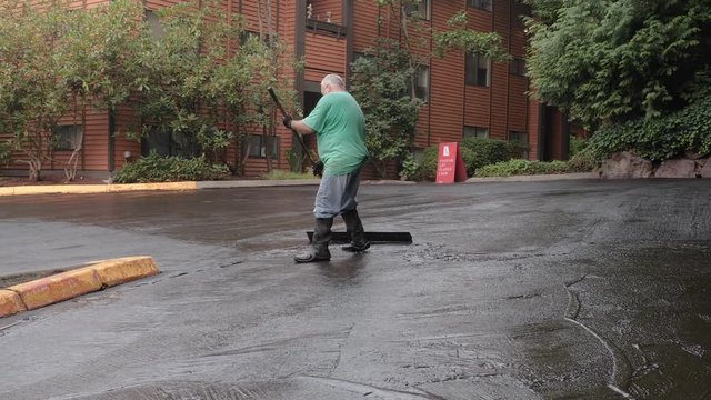 A blue-collar worker using a squeegee to spread seal coat mix.