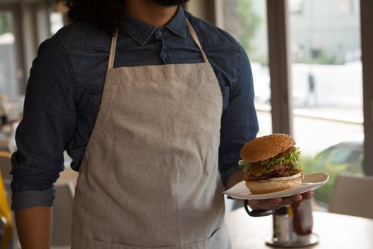 Waiter holding hamburger in cafe