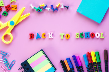 School supplies with coloured pen, scissors, binder clip, push pins, paper note, sticky note and wooden text BACK TO SCHOOL on pink background for education concept