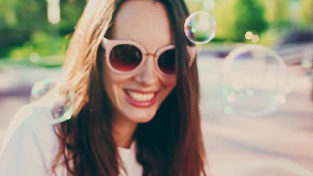 Portrait of young woman in sunglasses blowing bubbles and having fun on outdoors. Cinematic slow motion, young festival woman blowing bubbles, summer lifestyle
