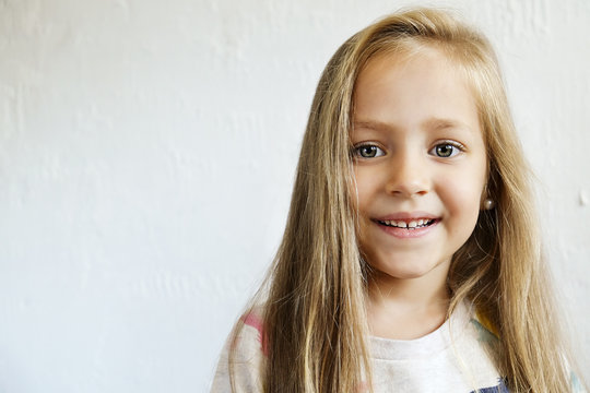 Portrait of happy little girl with long blonde hair smilng and showing positive emotions. Funny child with joyful facial expression. White isolated background, close up, copy space.